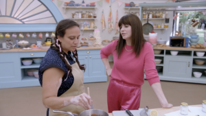 Jenn Reyes '99 talks with host Casey Wilson on the London set of 'The Great American Baking Show.' The pink ribbons in Reyes' braids speak to the korovai she made in tribute to her mother's anniversary of beating breast cancer. The creation earned her 'star baker' status on the episode, and the first person she called to tell was her mom.
